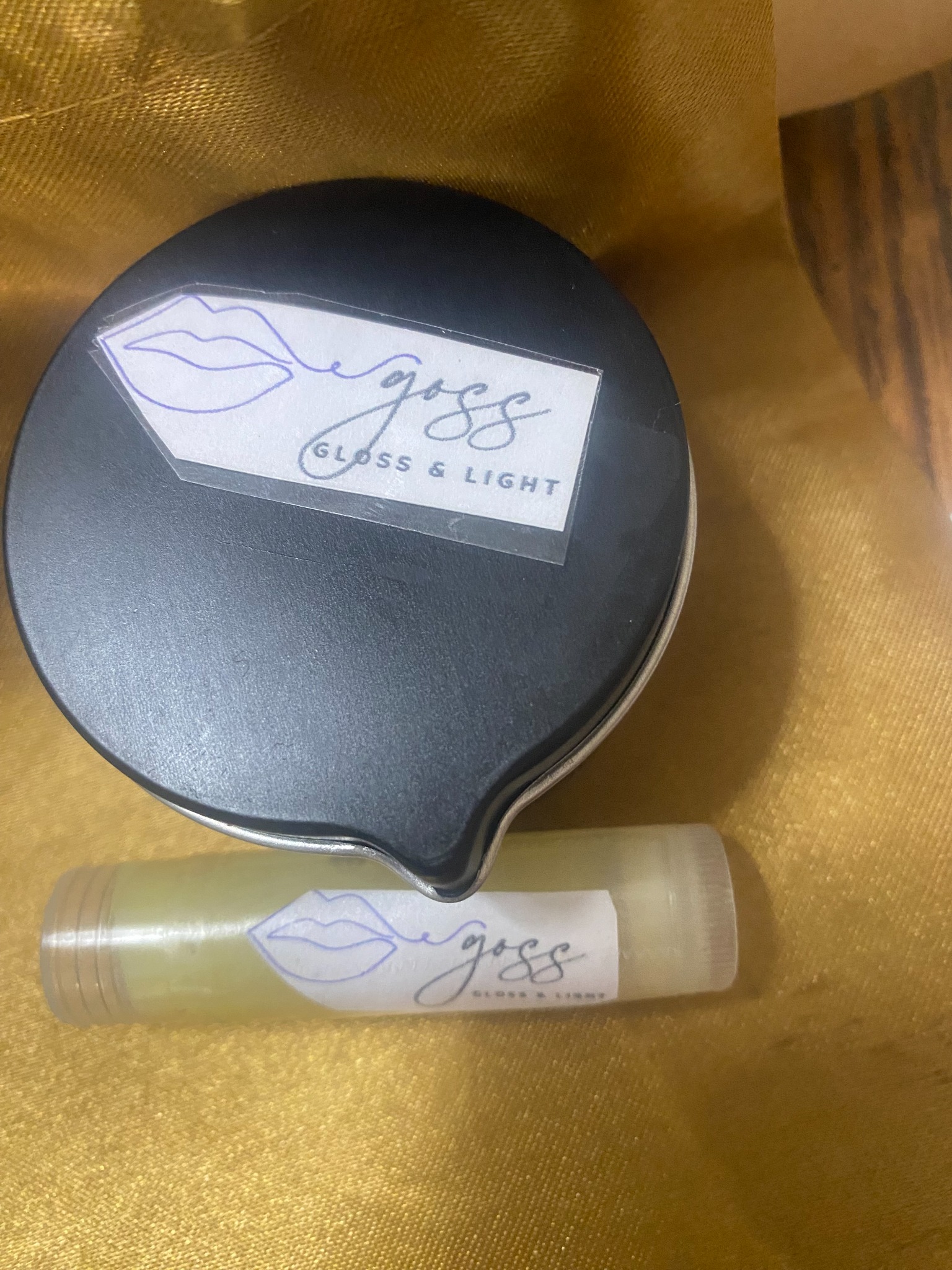 Goss Gloss & Light massage candle and lip product on gold fabric